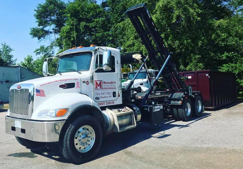 Photo of a Mercados Dumpster delivery truck dropping a dumpster off at a clients location.